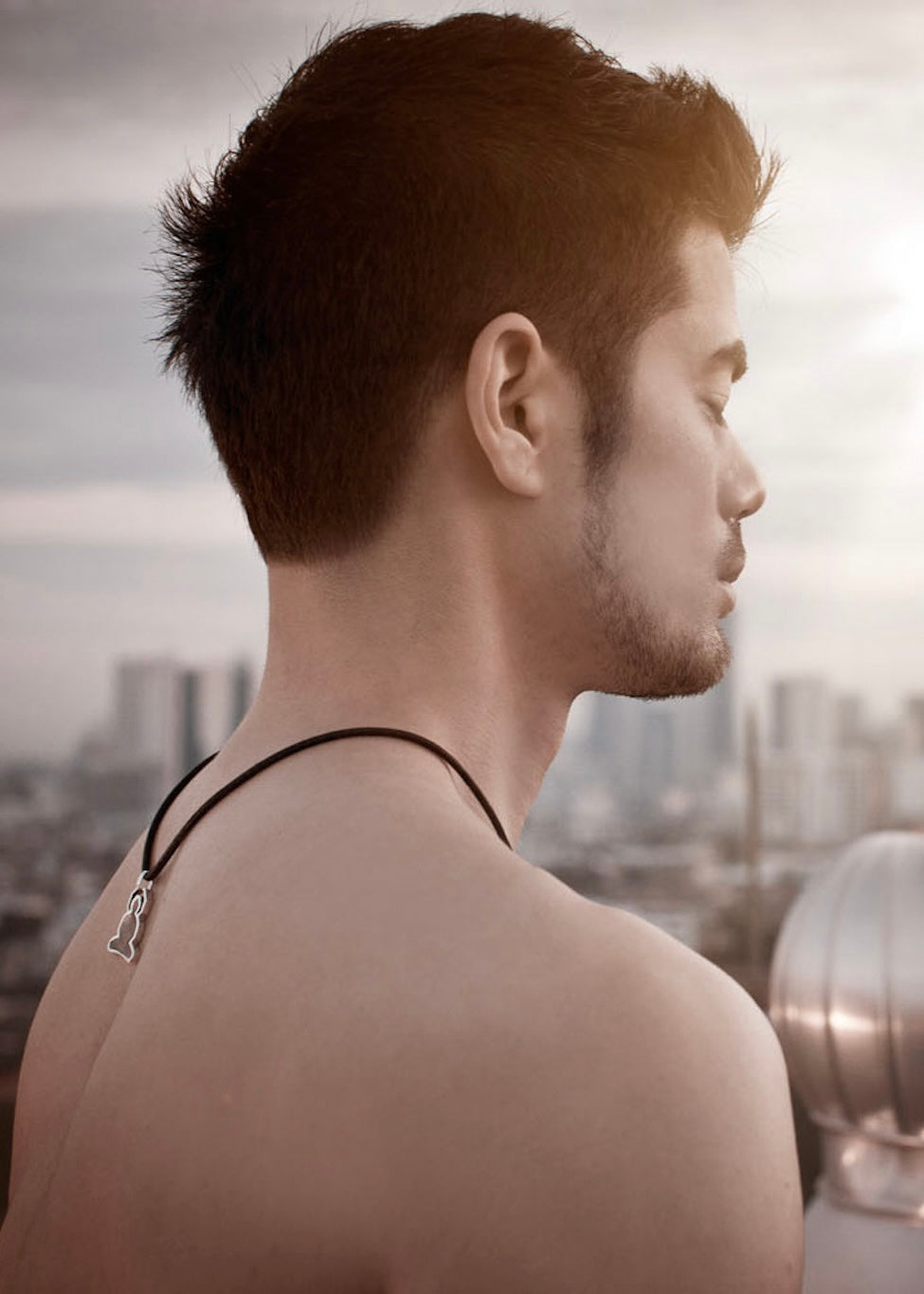 Man wearing a tigers and dragons buddha necklace looking over a cityscape