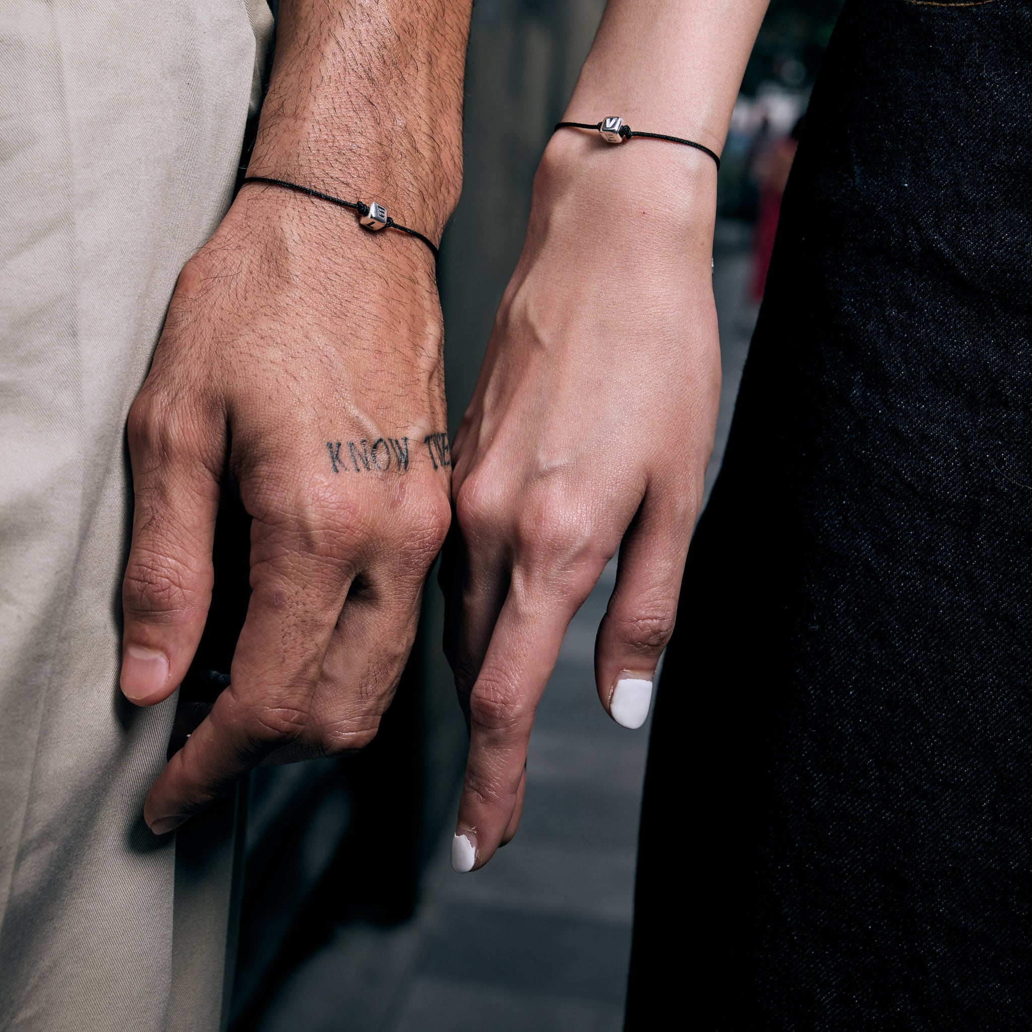 Close-up of two hands holding each other with tattoos and jewelry.