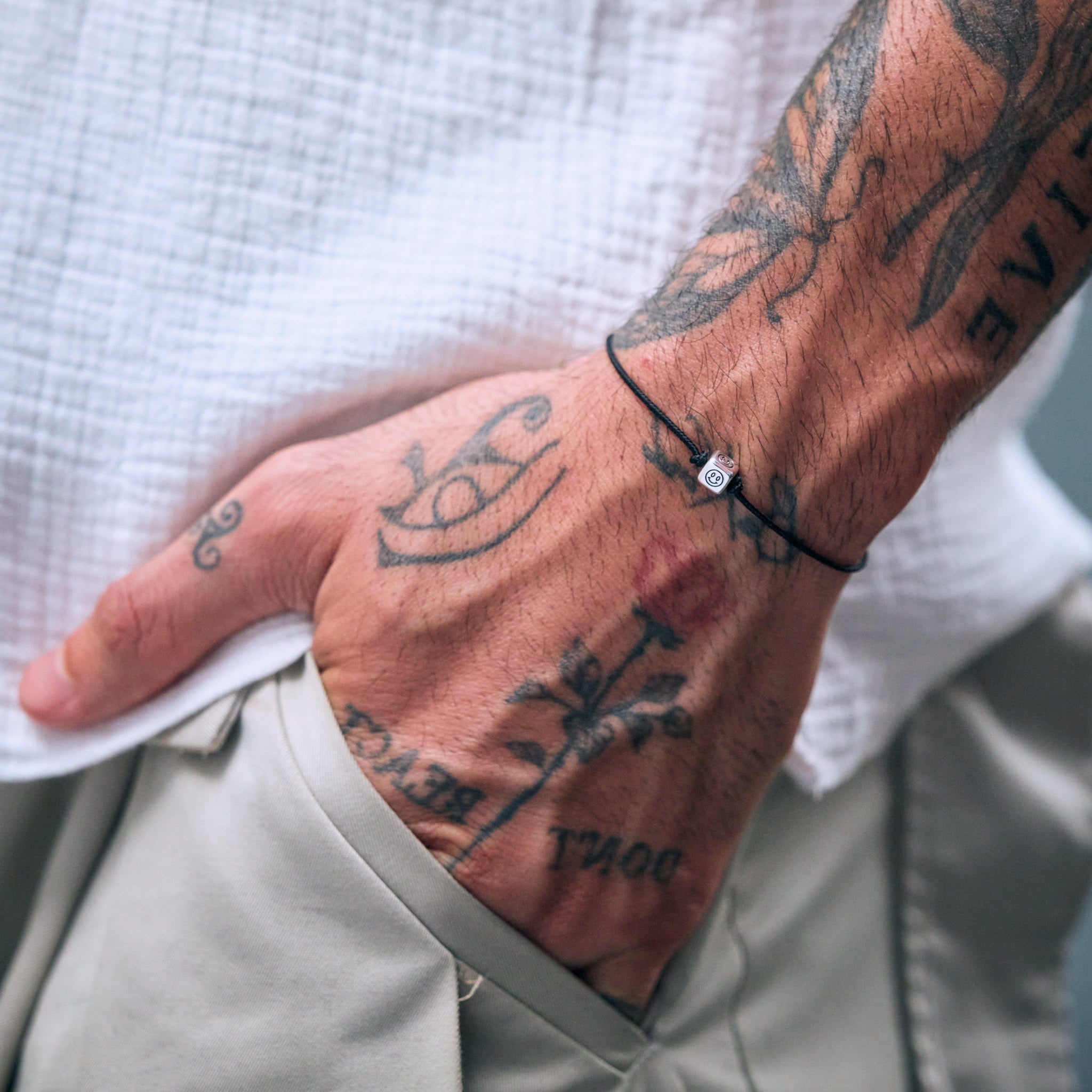 Male Model with tattoos on arm wearing a bracelet with a silver smiley charm