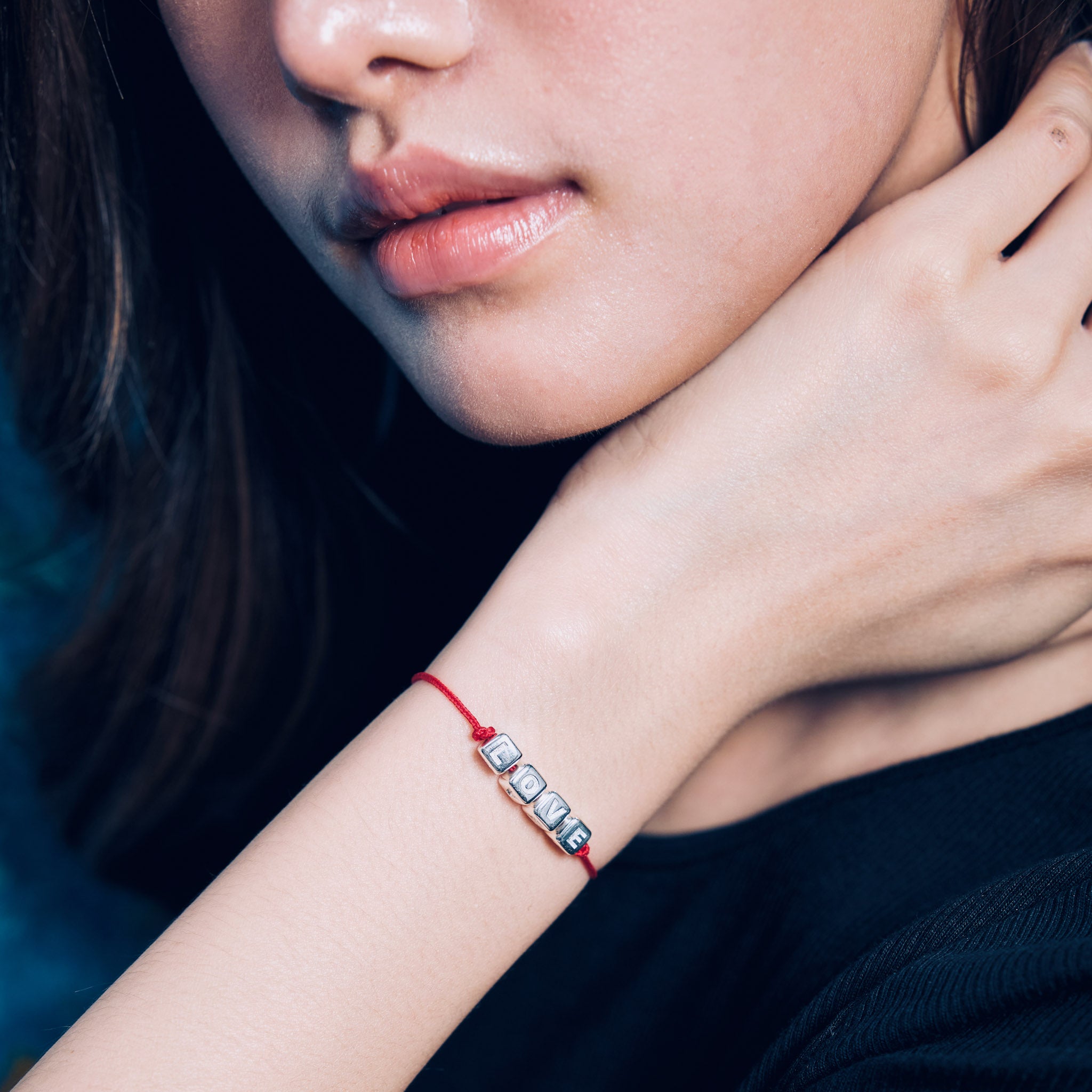 Close-up of a person wearing a red bracelet with small silver love cube charms.