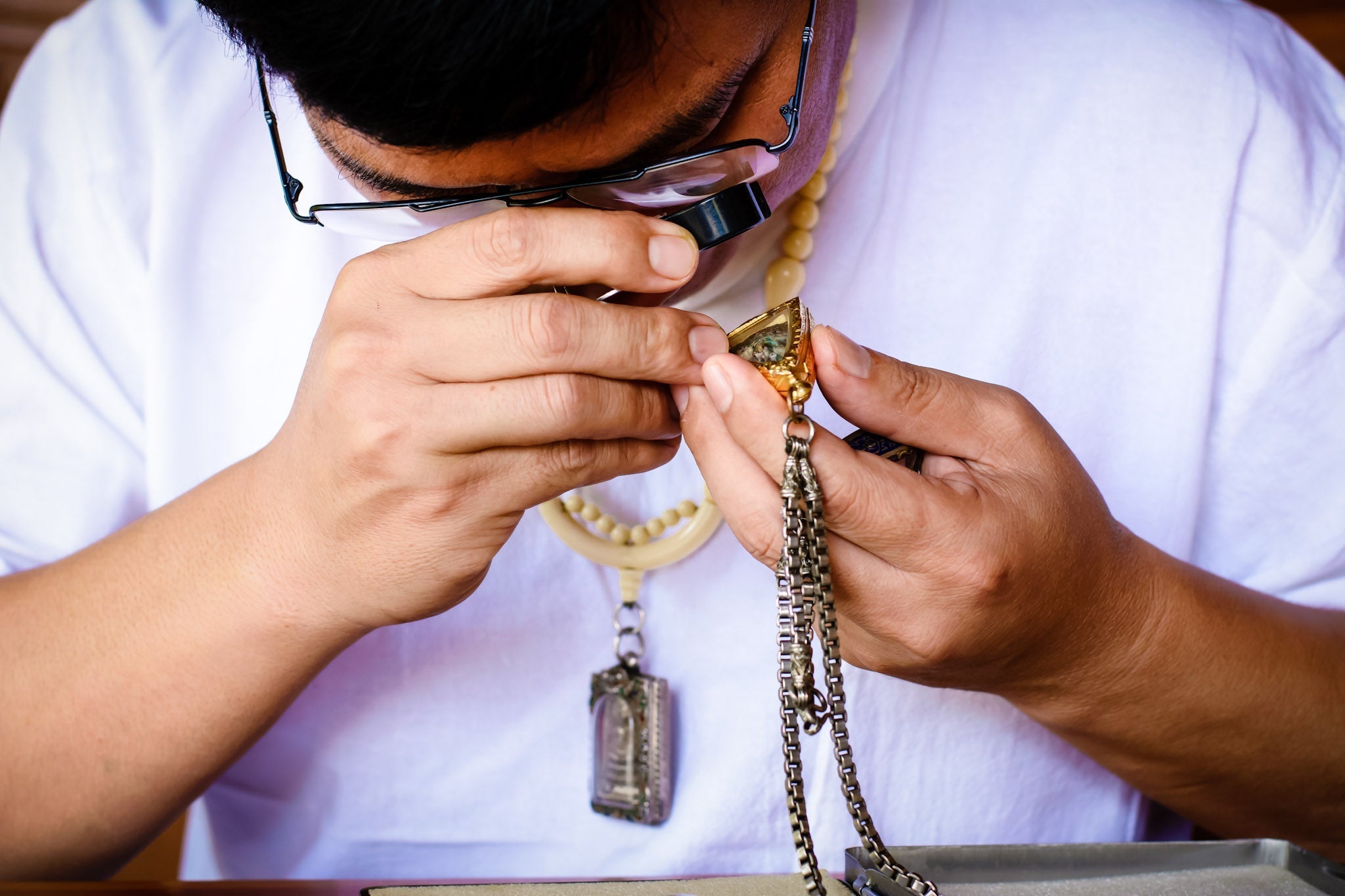 Thai man inspecting a buddha amulet with a jewelry loupe